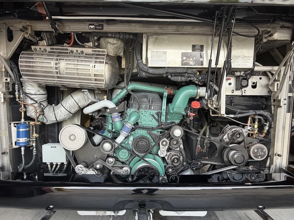 Inner engine compartment of an RV showing various engine components, belts, pulleys, hoses, and wiring.