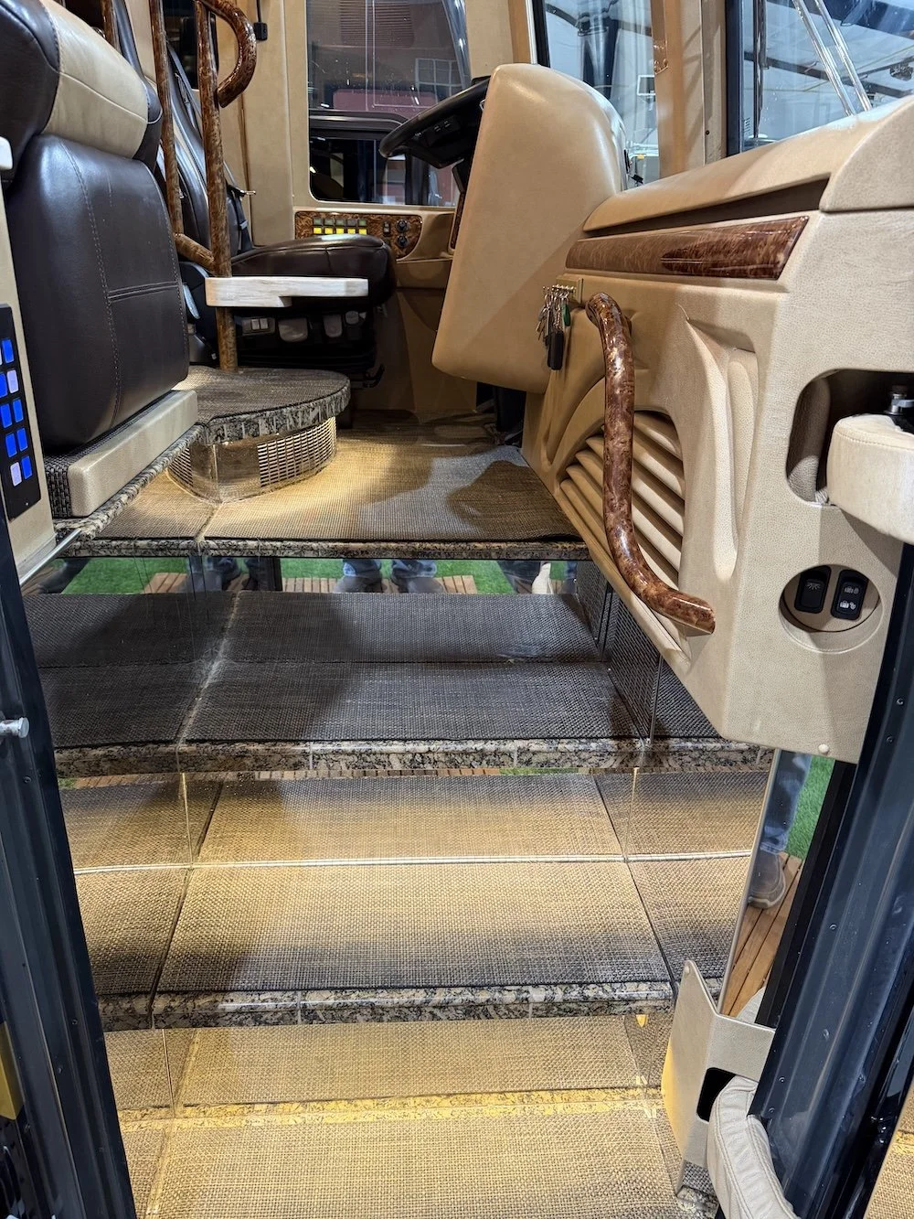 Interior of a RV with steps, beige and brown colored dashboard, and seats. 