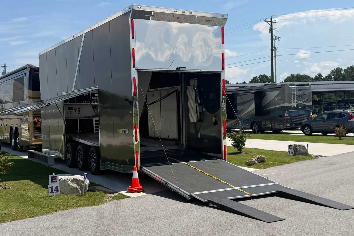 Rear view of the trailer with ramp extended, parked beside a motorcoach
