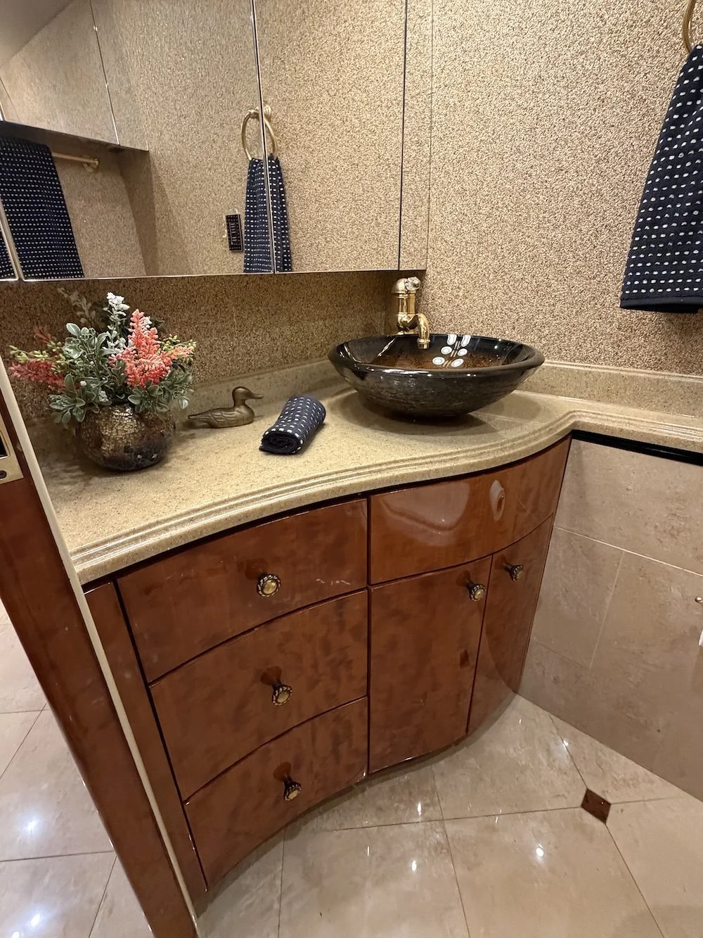 Close-up of the bathroom counter, black glass vessel sink, and gold faucet.