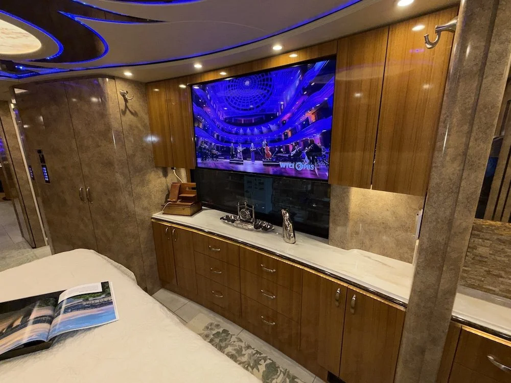 RV master bedroom with a large flat-screen TV mounted above a wooden cabinet, a marble countertop.