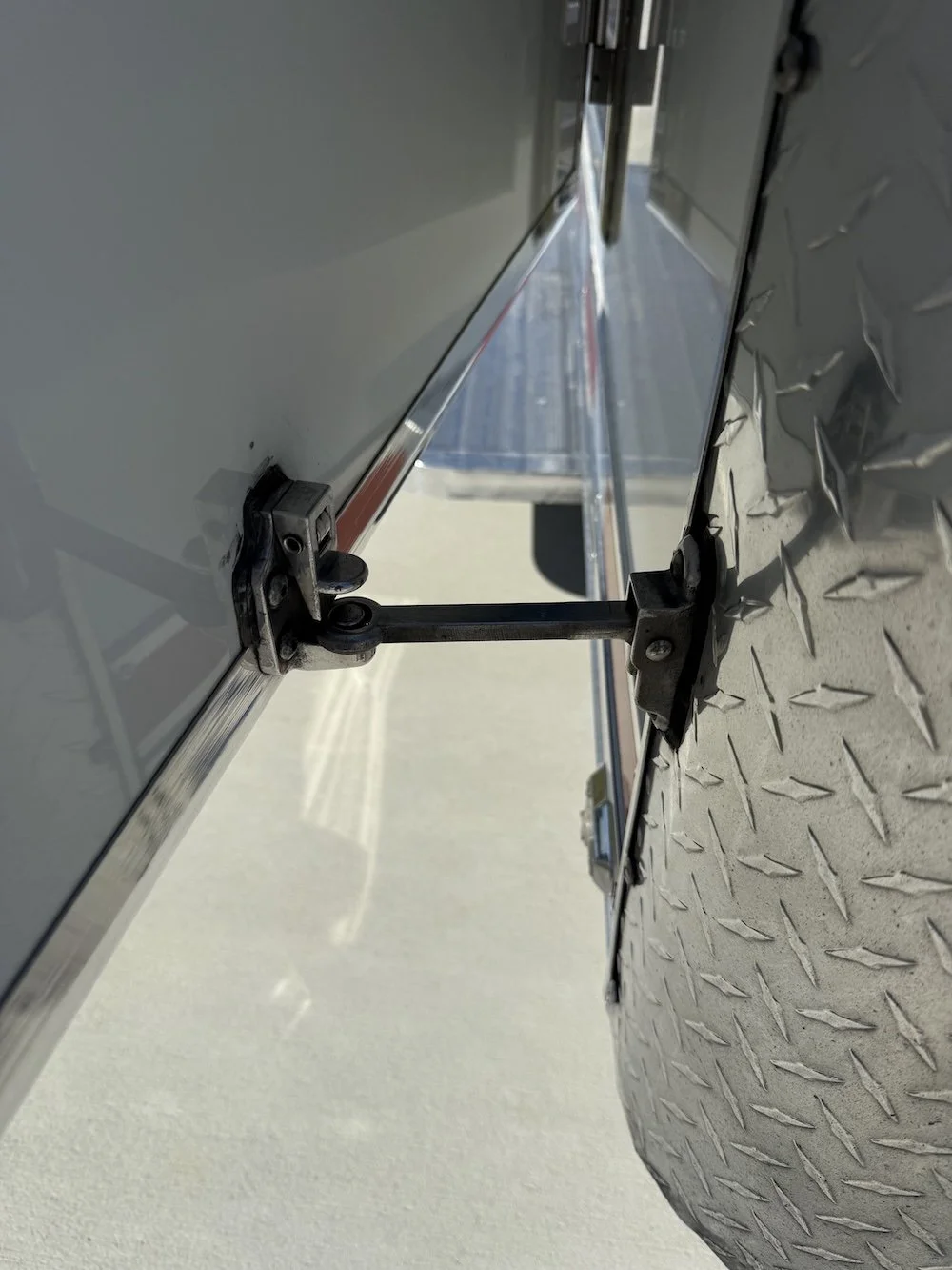 Close-up of the hinge mechanism connecting a metal panel to a truck trailer, showing the textured diamond plate surface underneath.