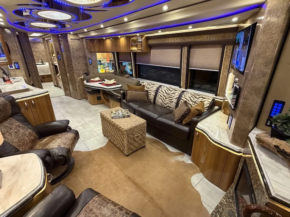 Interior of a luxury RV with a leather sofa, zebra-print fabric, and wood-paneled walls, featuring a small dining or work table.