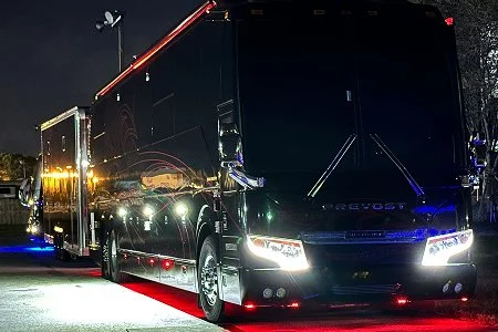 Side profile of a motorcoach parked at night featuring vibrant red awning and undercarriage LED
