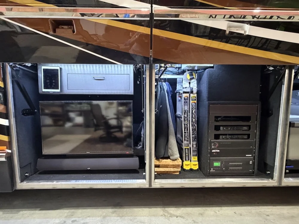 View of a service compartment inside an RV, featuring a television, a small drawer, a mounted tablet, and various tools and electronic equipment.