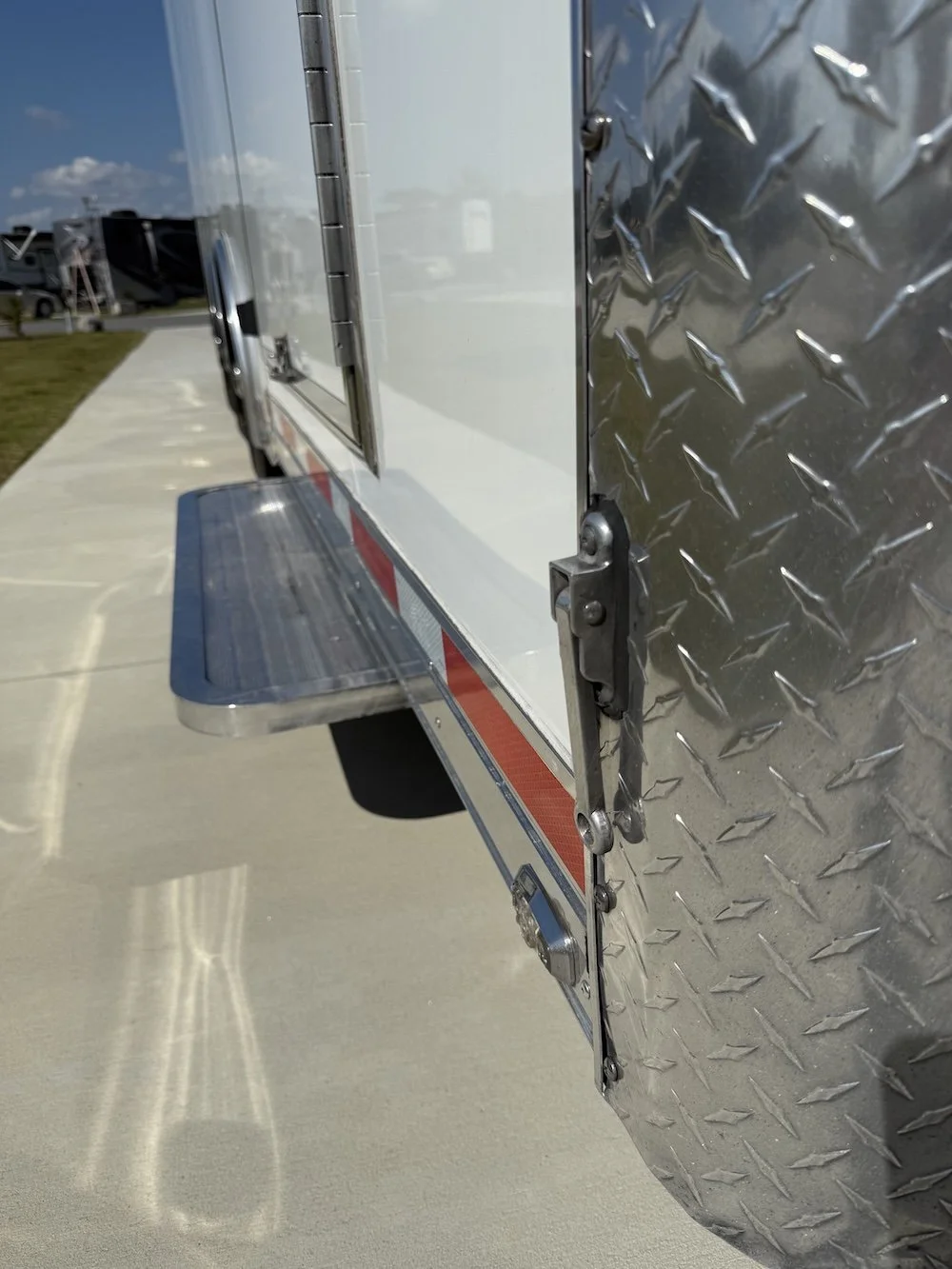 Close-up of a side of a white utility truck with a diamond plate steel panel, a step, and a lock mechanism.