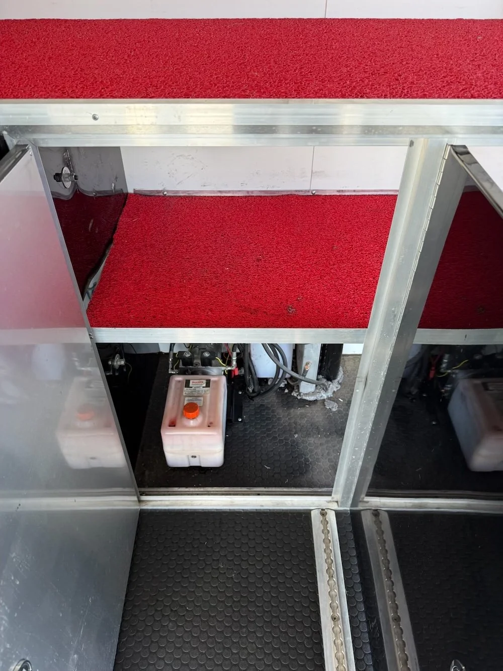 Empty red-carpeted display case with metal framing and a small plastic container with a orange cap on the bottom shelf.