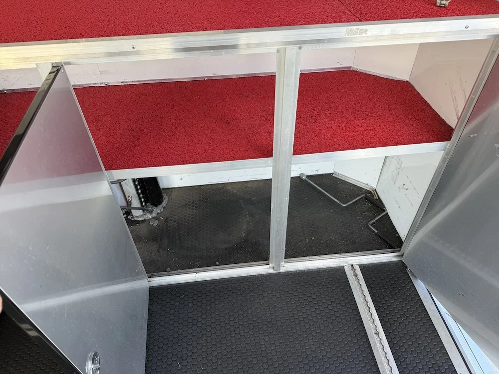 View inside a small metal structure with black rubber flooring, red carpeted platform, and a small support beam freestanding in the middle.