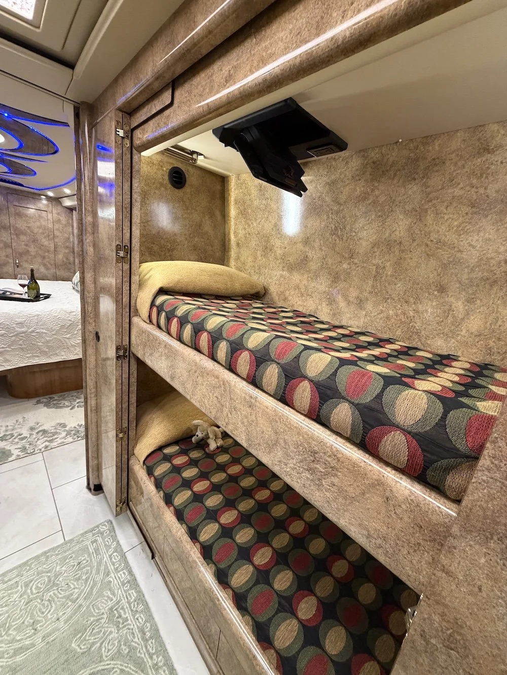 Bunk beds with polka dot bedding in a small, cozy room, with a small TV mounted above, and a plush pillow on the top bunk.
