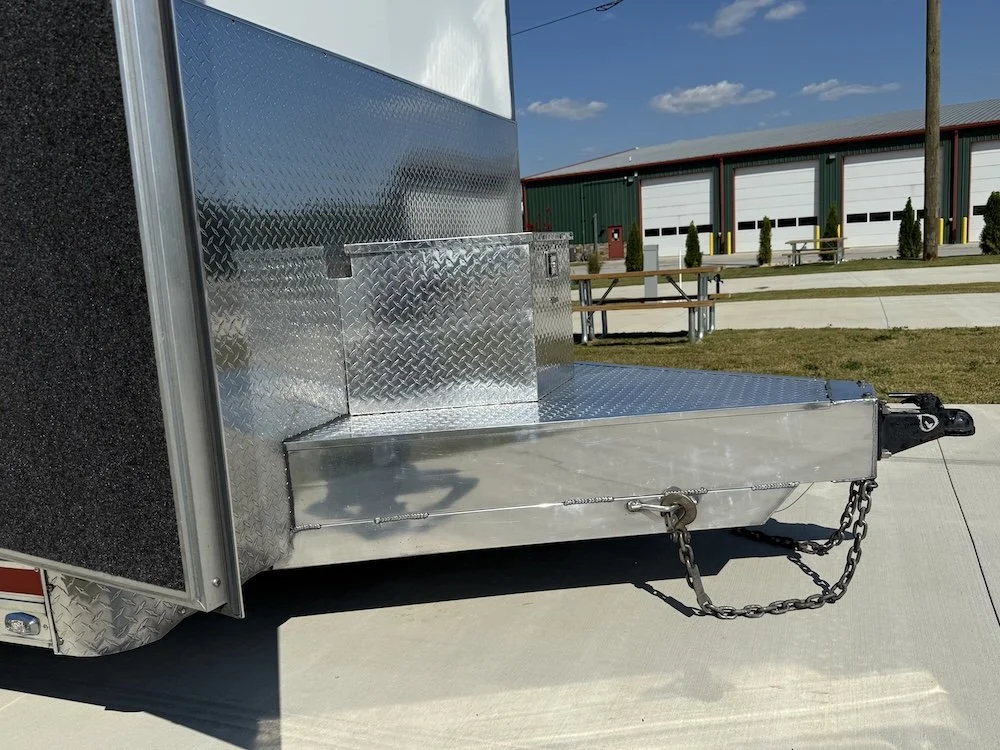 Close-up of a metallic utility trailer hitch with chains and a lock in a parking lot.