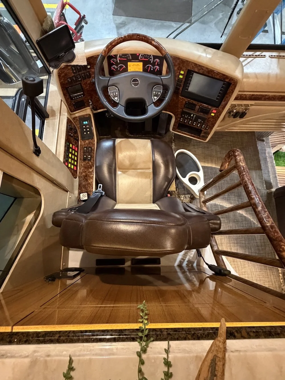Overhead view of an RV driver's seat and dashboard with steering wheel, electronic controls, and navigation screen.