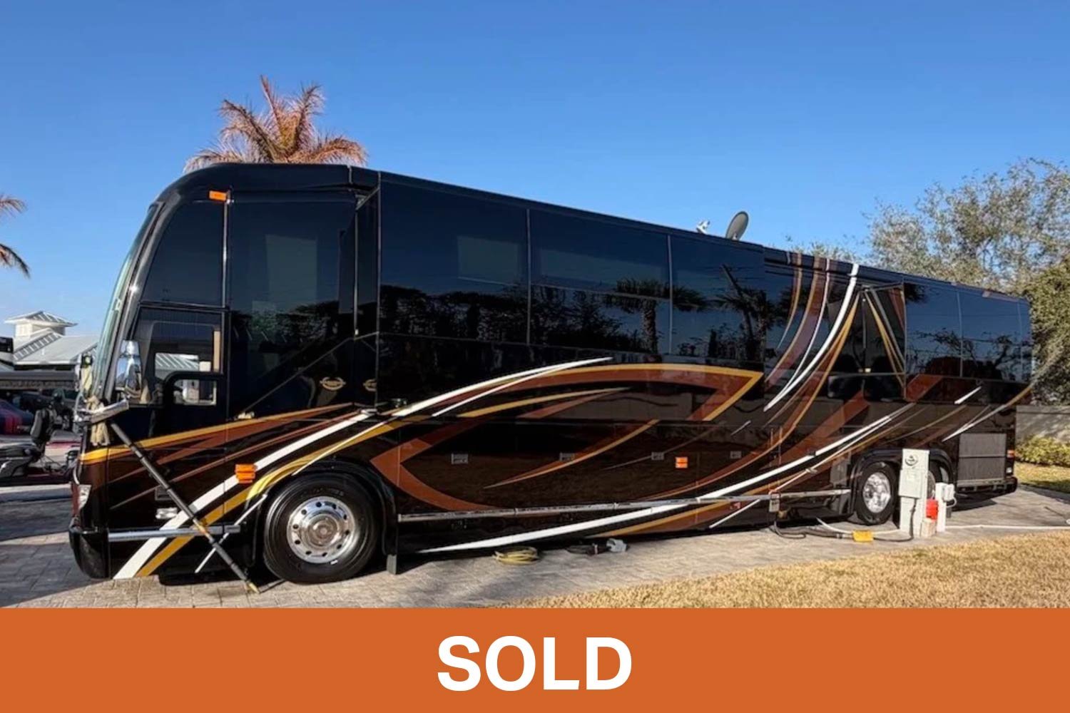 Angled front view of a black and copper 2016 Marathon luxury coach parked at a campsite.