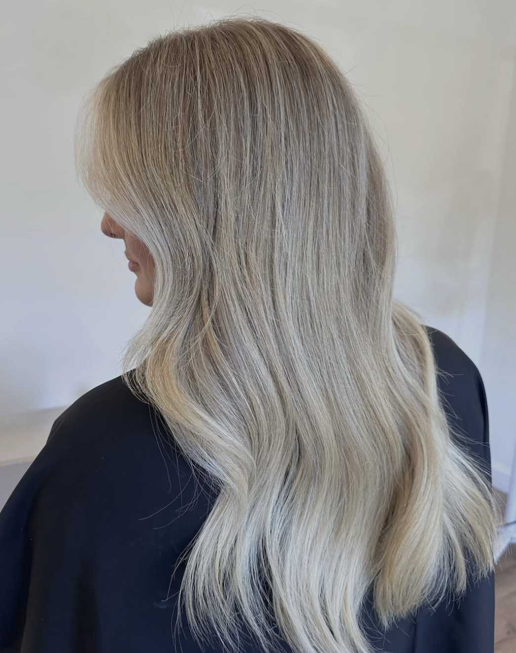 Woman with long, wavy blonde hair looking to the side, wearing a black top.