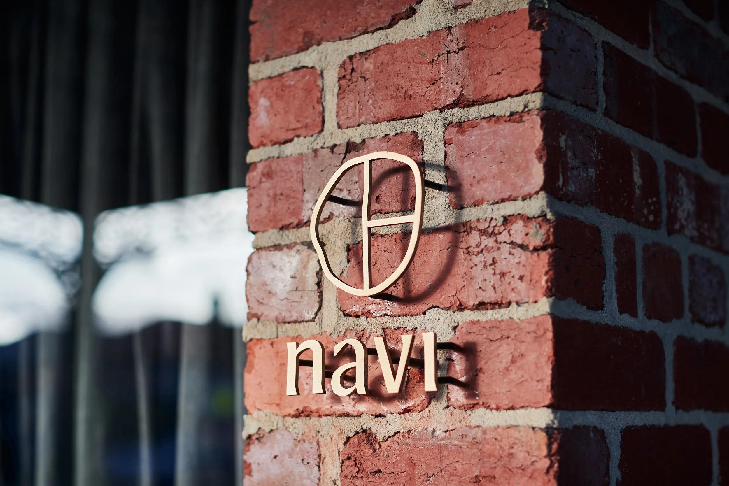Close-up of a brick wall with a white sign that says 'navigate' mounted on it, casting a shadow.