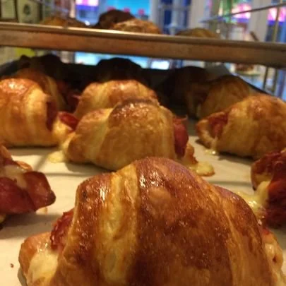 Freshly baked croissants filled with ham and cheese on a baking tray in a pastry shop.