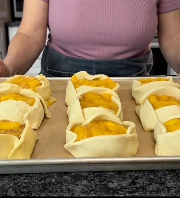 Unbaked peach galettes on a baking sheet in a kitchen.