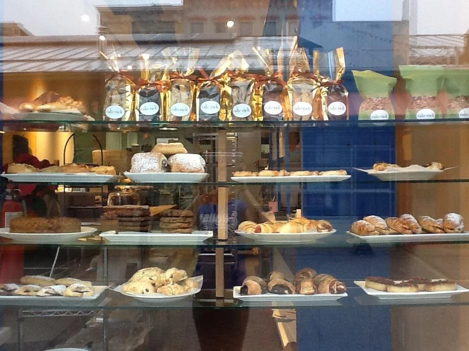 Bakery window display with an assortment of pastries, breads, and packaged snacks on glass shelves.