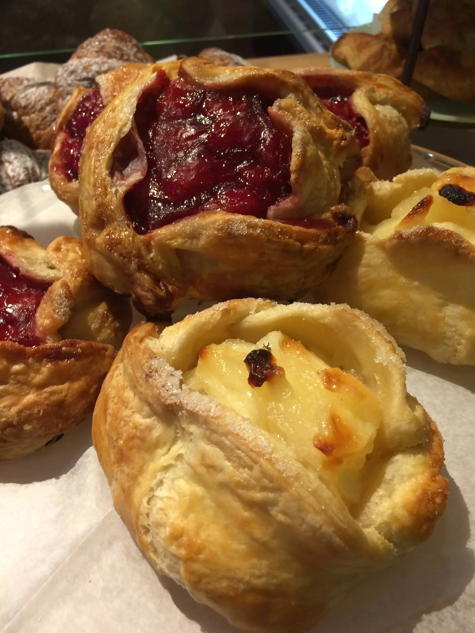 Freshly baked pastries with fruit fillings, including red berry and apple, displayed on a tray.