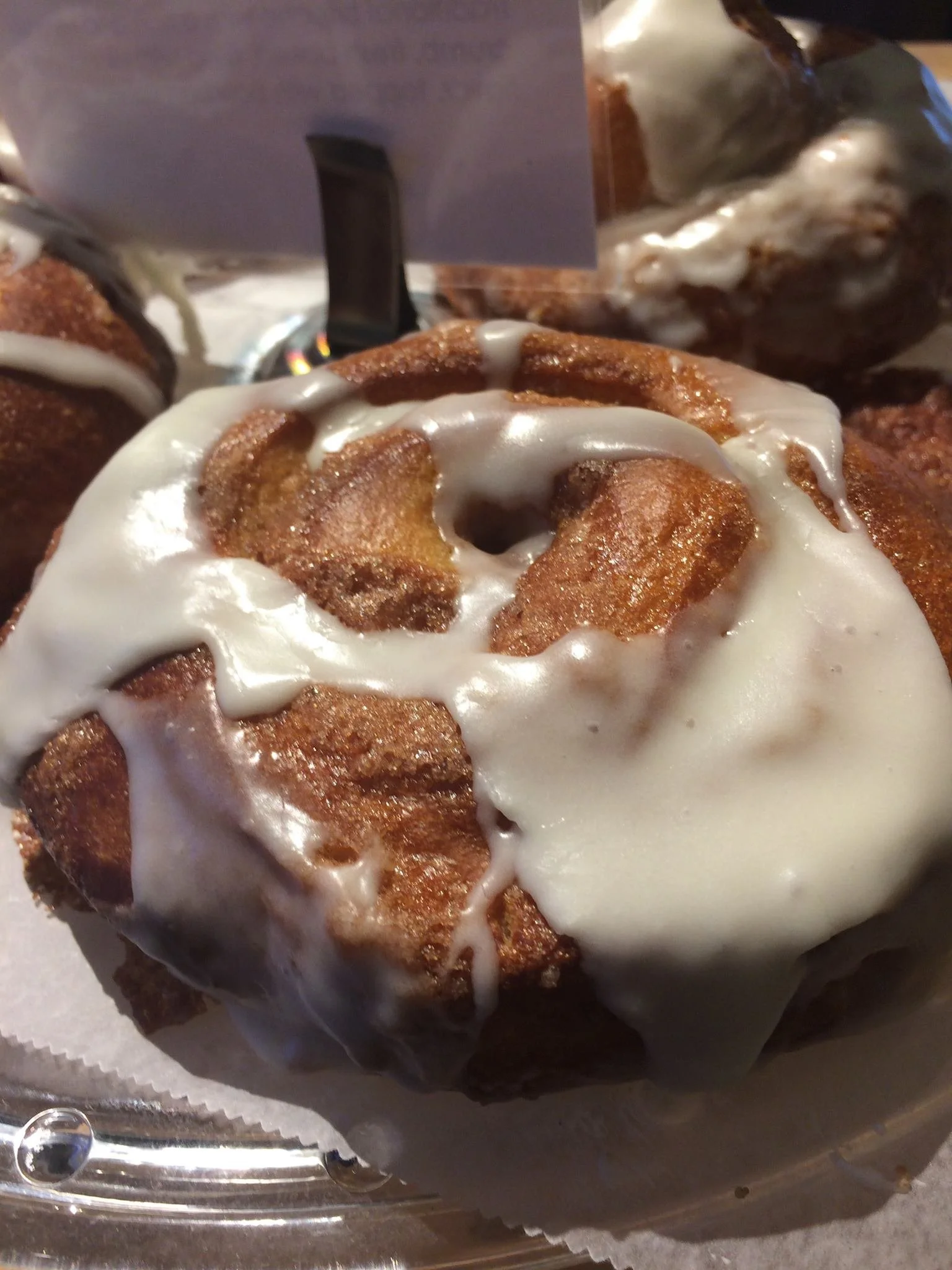 Close-up of a cinnamon roll topped with white icing, displayed on a surface.