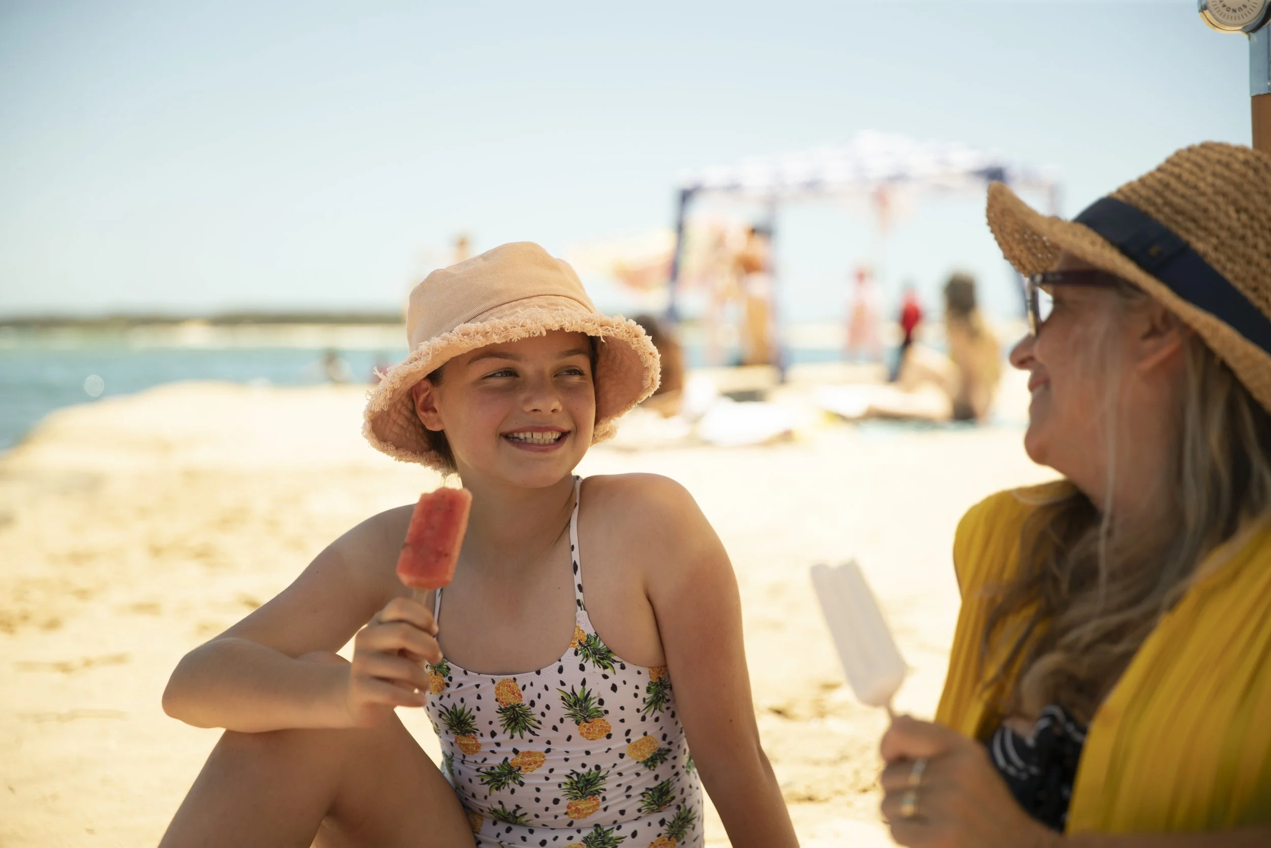 Woman and child sitting on the beach with big smiles as they enjoy their Frozen Sunshine iceblocks