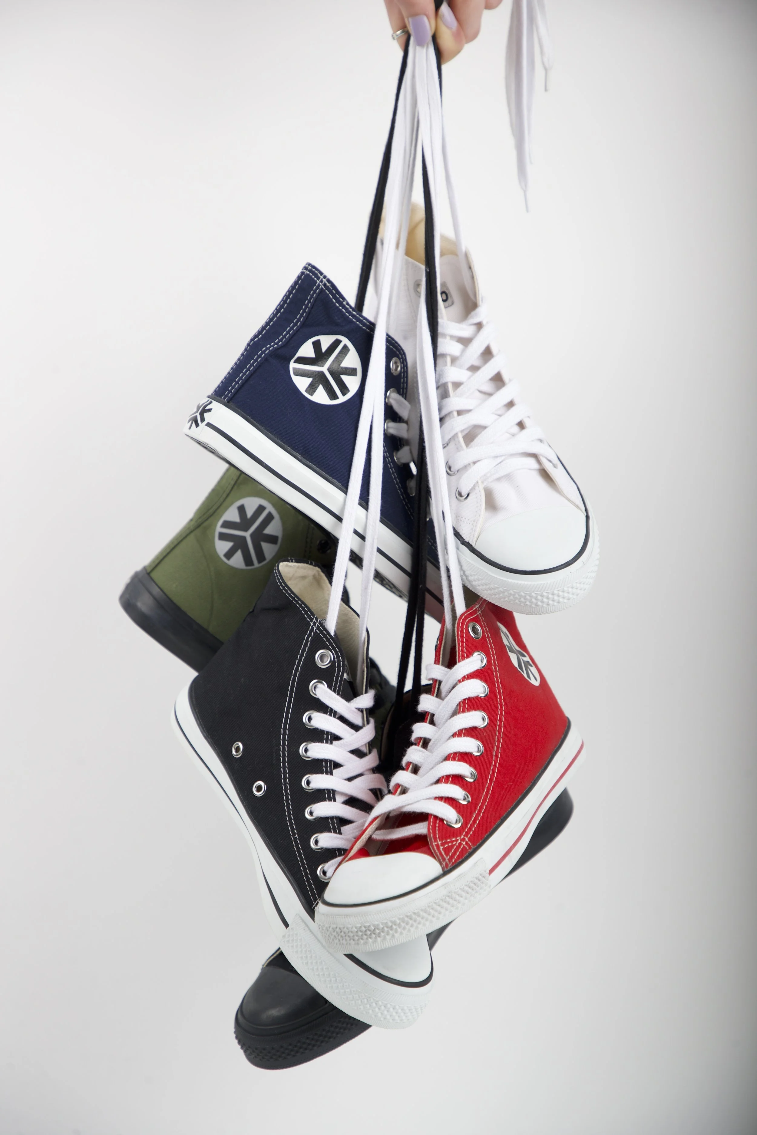 Multiple colorful sneakers hanging by their laces against a plain background.