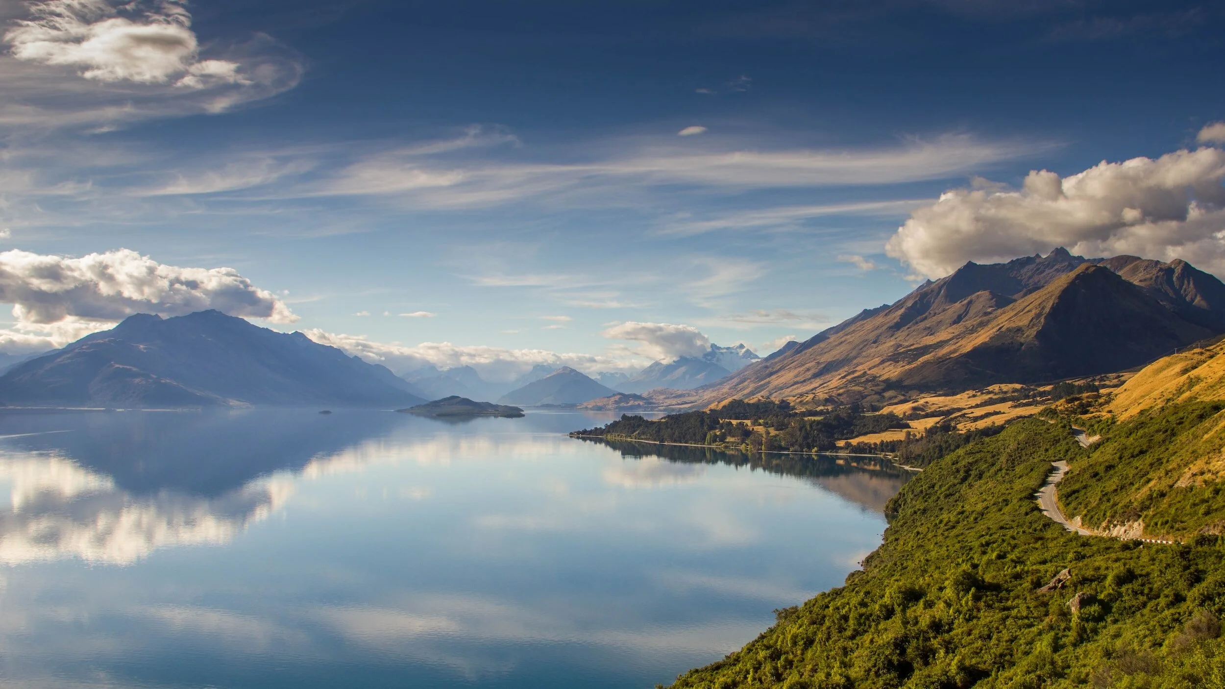 Scenic lake with surrounding mountains and cloudy sky reflecting on the water.