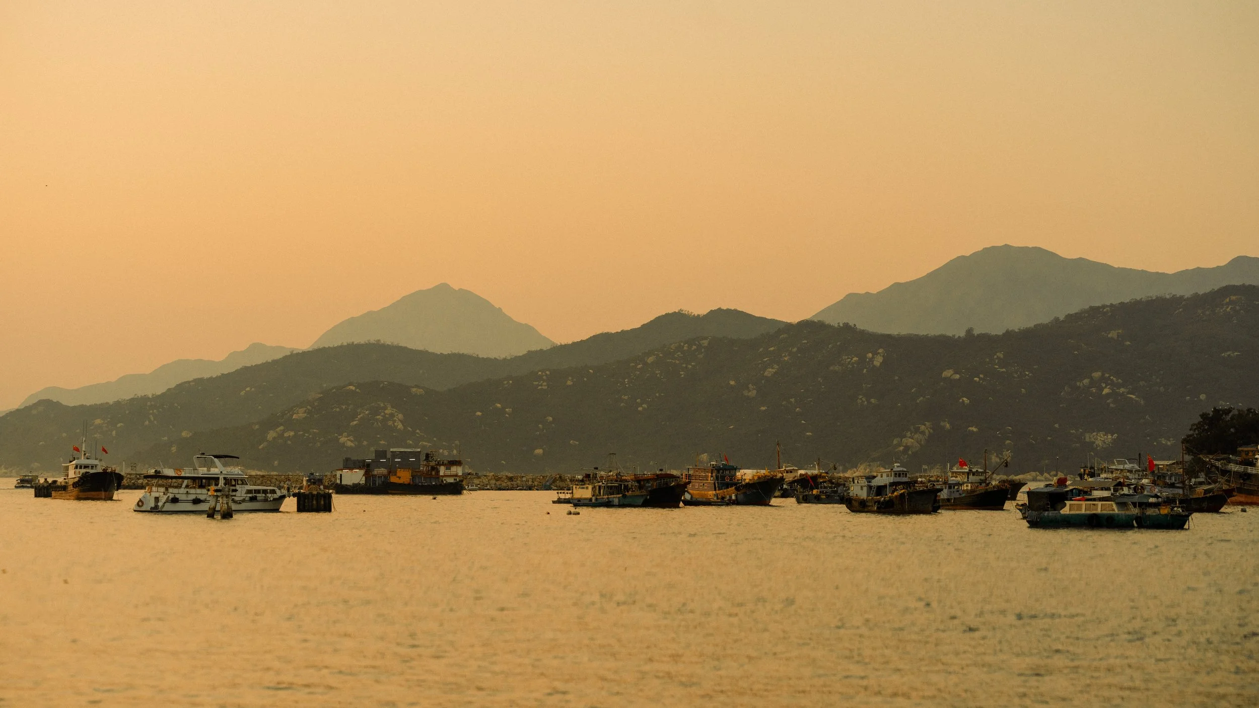 Boats docked at a harbor with mountains in the background during sunset.