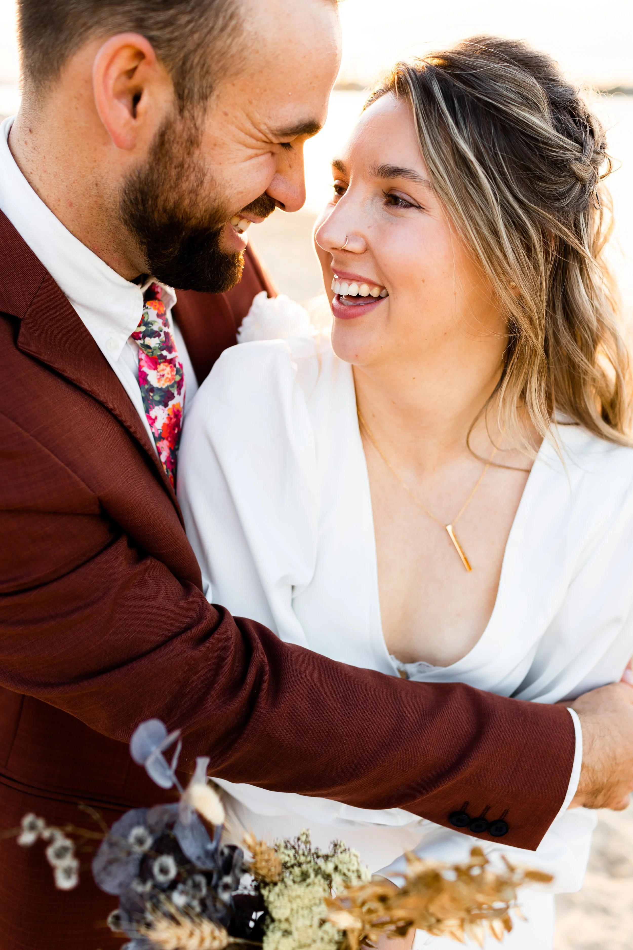 A happy couple smiling and embracing outdoors, with the woman holding a bouquet of flowers.