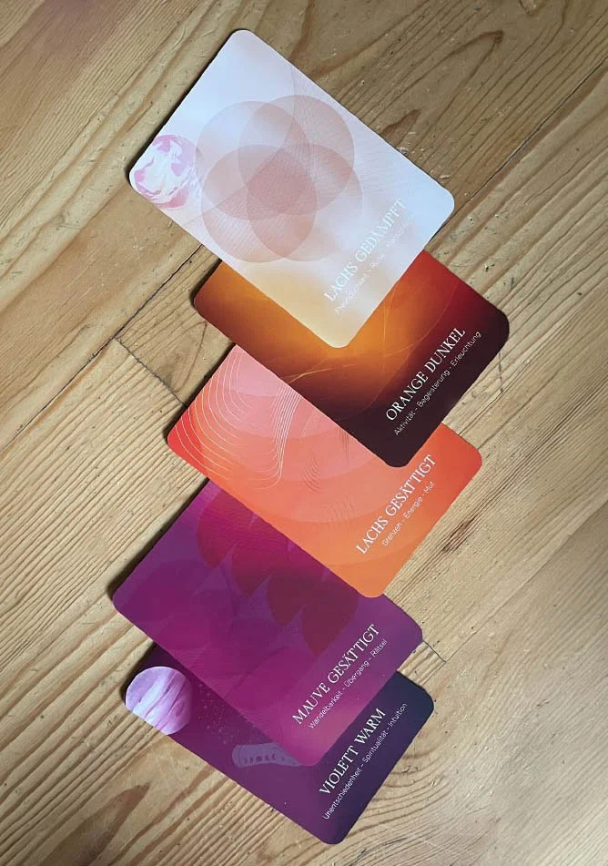 Fünf Karten in verschiedenen Farben und Designs, die mit positiven Gefühlszuständen verbunden sind, auf einem Holztisch.