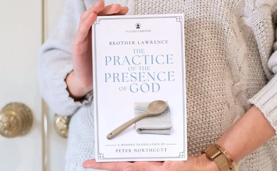 Person holding a book titled 'The Practice of the Presence of God' by Brother Lawrence, translated by Peter Northcutt.
