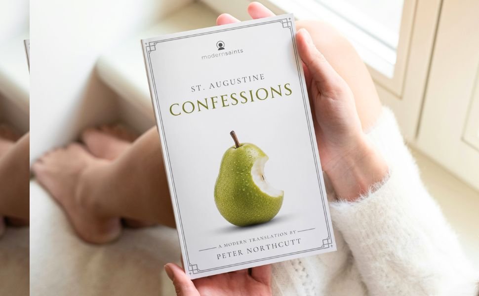 A person holding a book titled 'Confessions: a modern translation' by St. Augustine, featuring a green pear with a bite taken out on the cover, near a window.