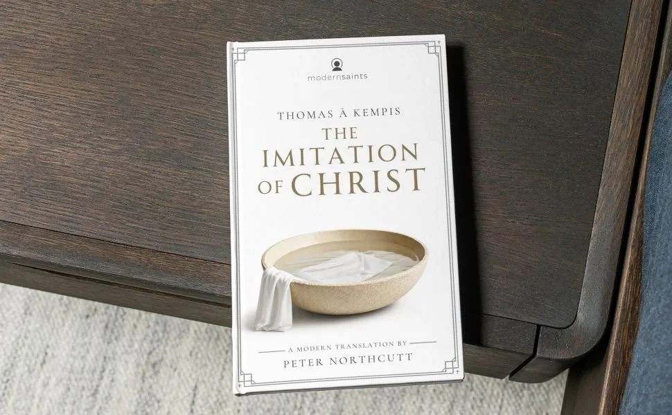 Book titled 'The Imitation of Christ' by Thomas à Kempis, translated by Peter Northcutt, placed on a dark wooden surface.