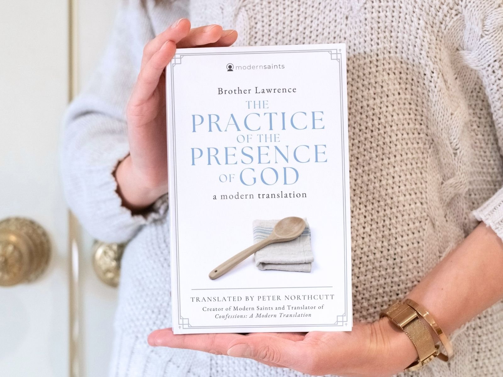 Person holding a book titled 'The Practice of the Presence of God' by Brother Lawrence, translated by Peter Northcutt.