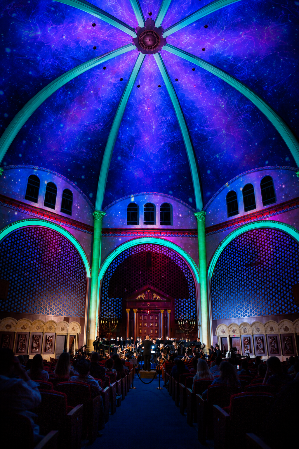 An orchestra performs beneath a dome illuminated in violet, blue and teal at Temple Emanu-El