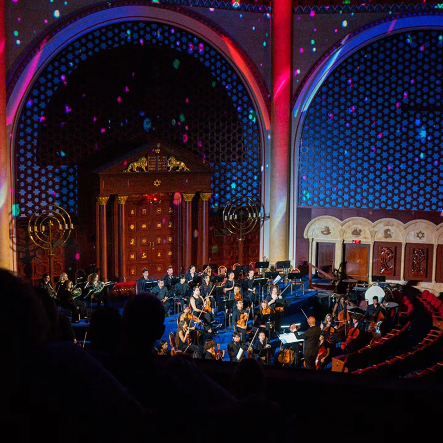Audience view of musicians surrounded by blue and magenta architectural lighting