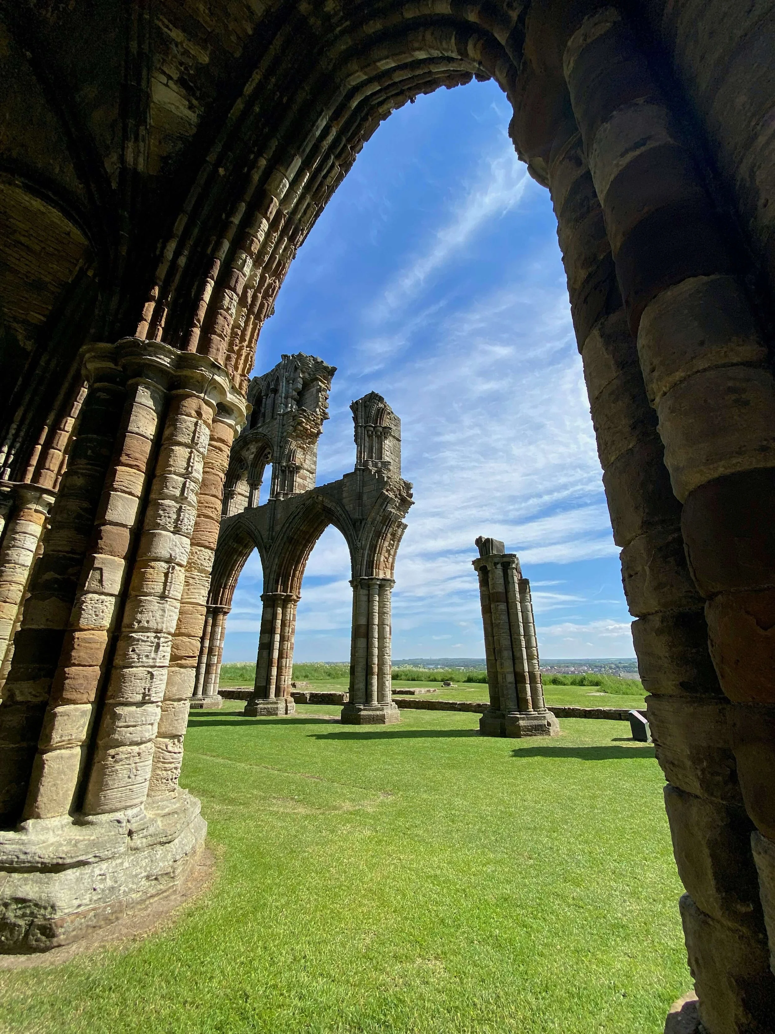 Ruins of an ancient stone archway with columns on a grassy field under a blue sky.