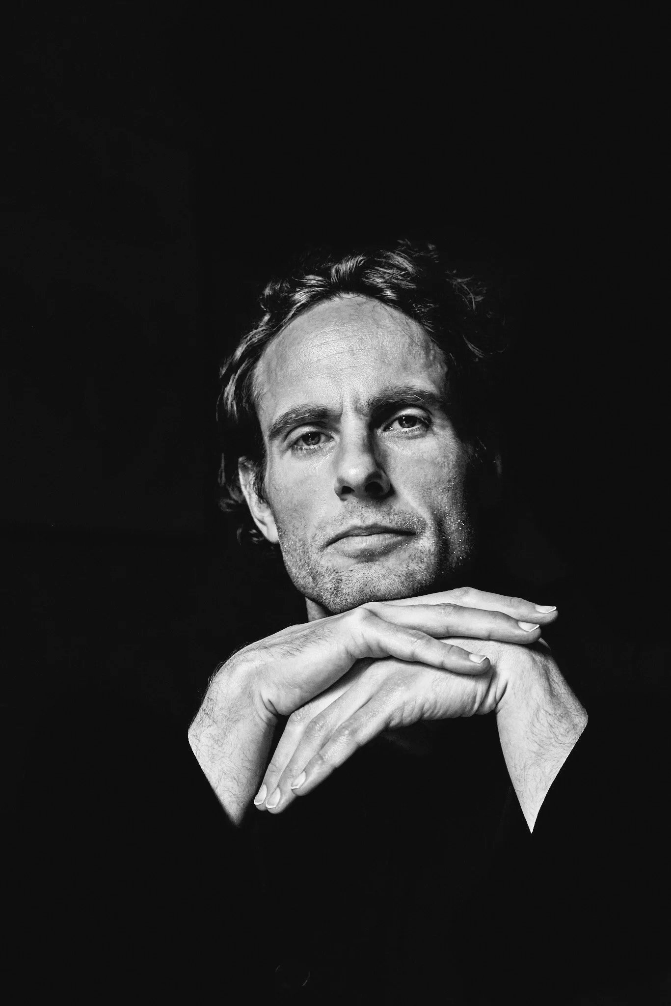 Black and white portrait of a man with folded hands.