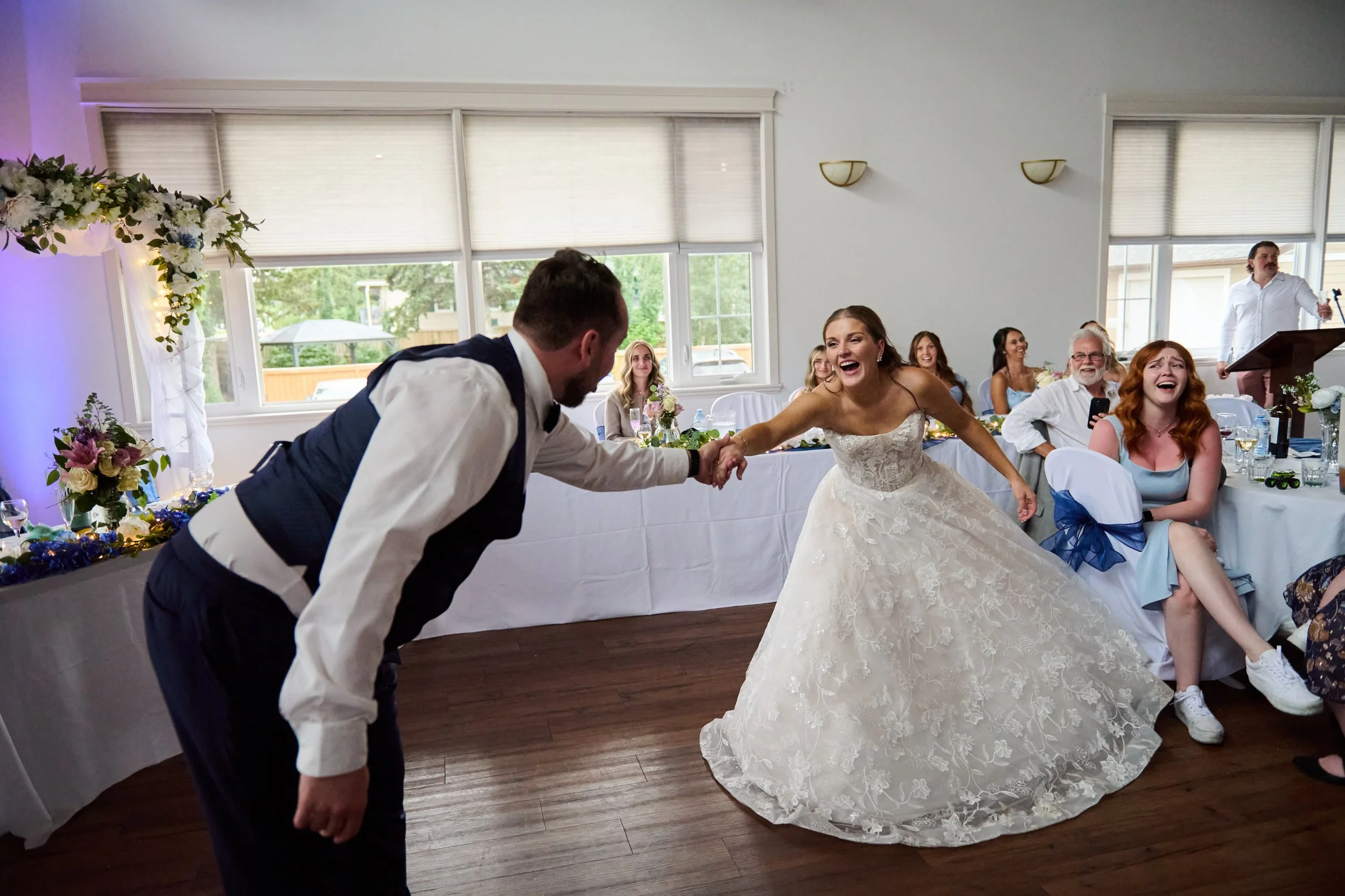 Bride and groom dancing at wedding reception with guests watching and smiling.