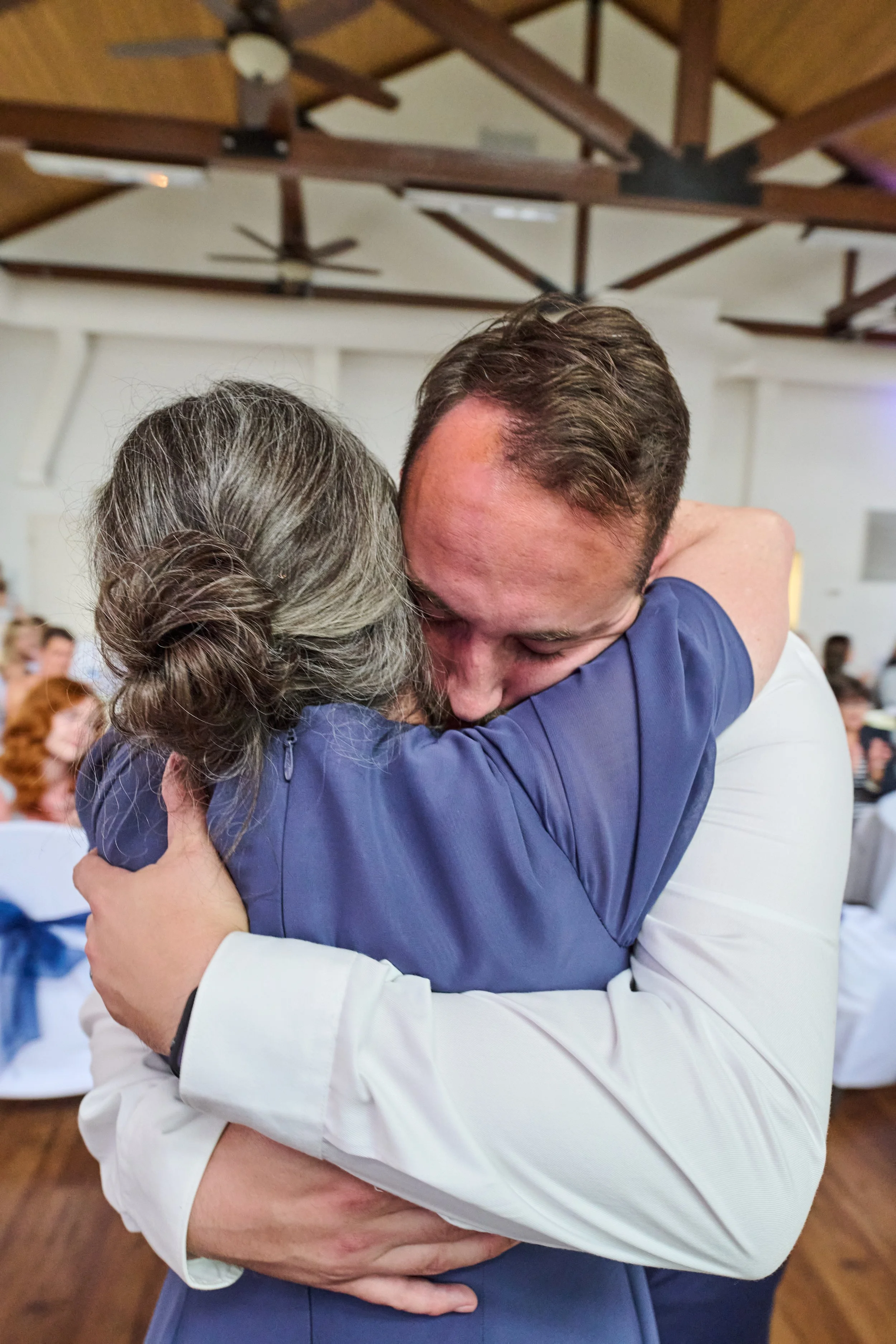 A woman and a man sharing an emotional hug at a celebration event with other guests in the background.
