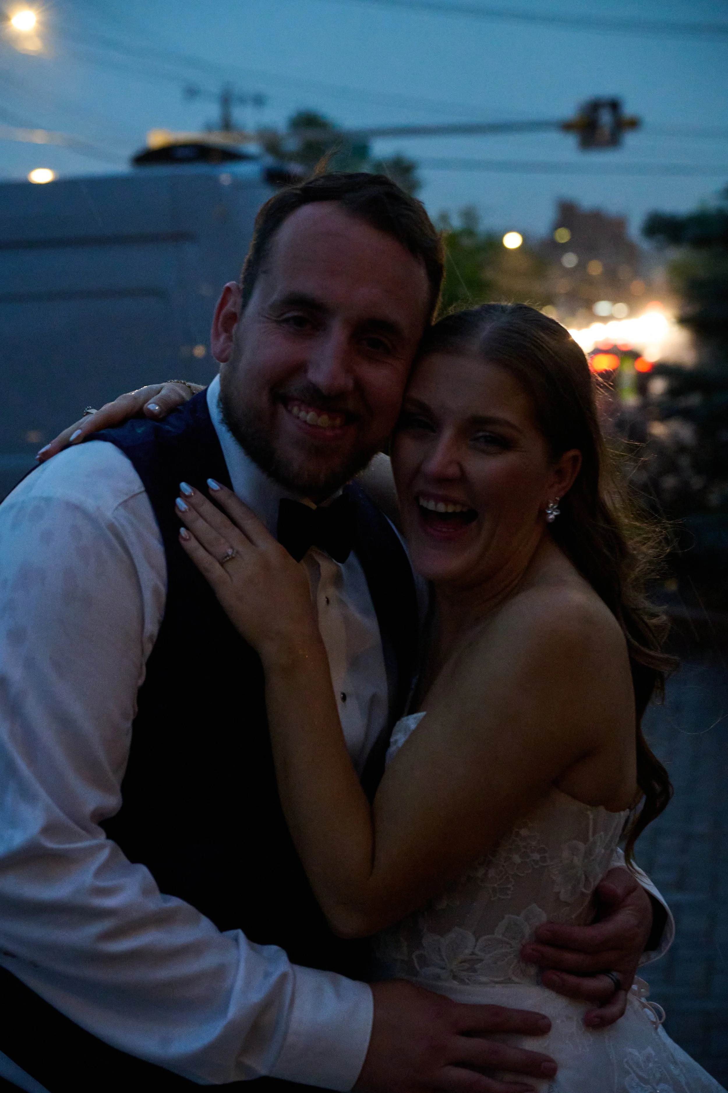 Happy bride and groom embracing at sunset, smiling with joyful expressions.