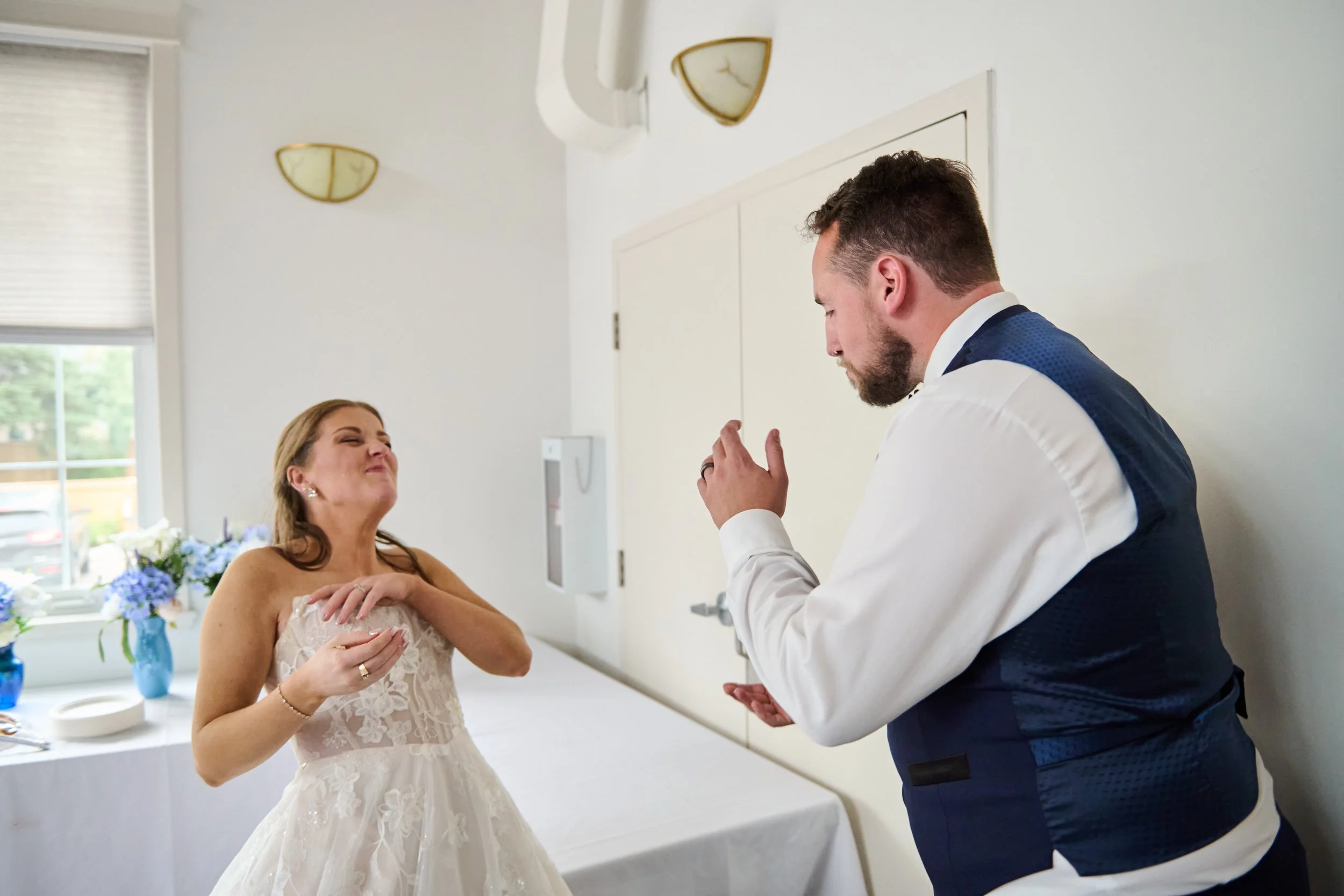 A bride and groom in a room, making playful and emotional expressions, possibly during a wedding celebration.