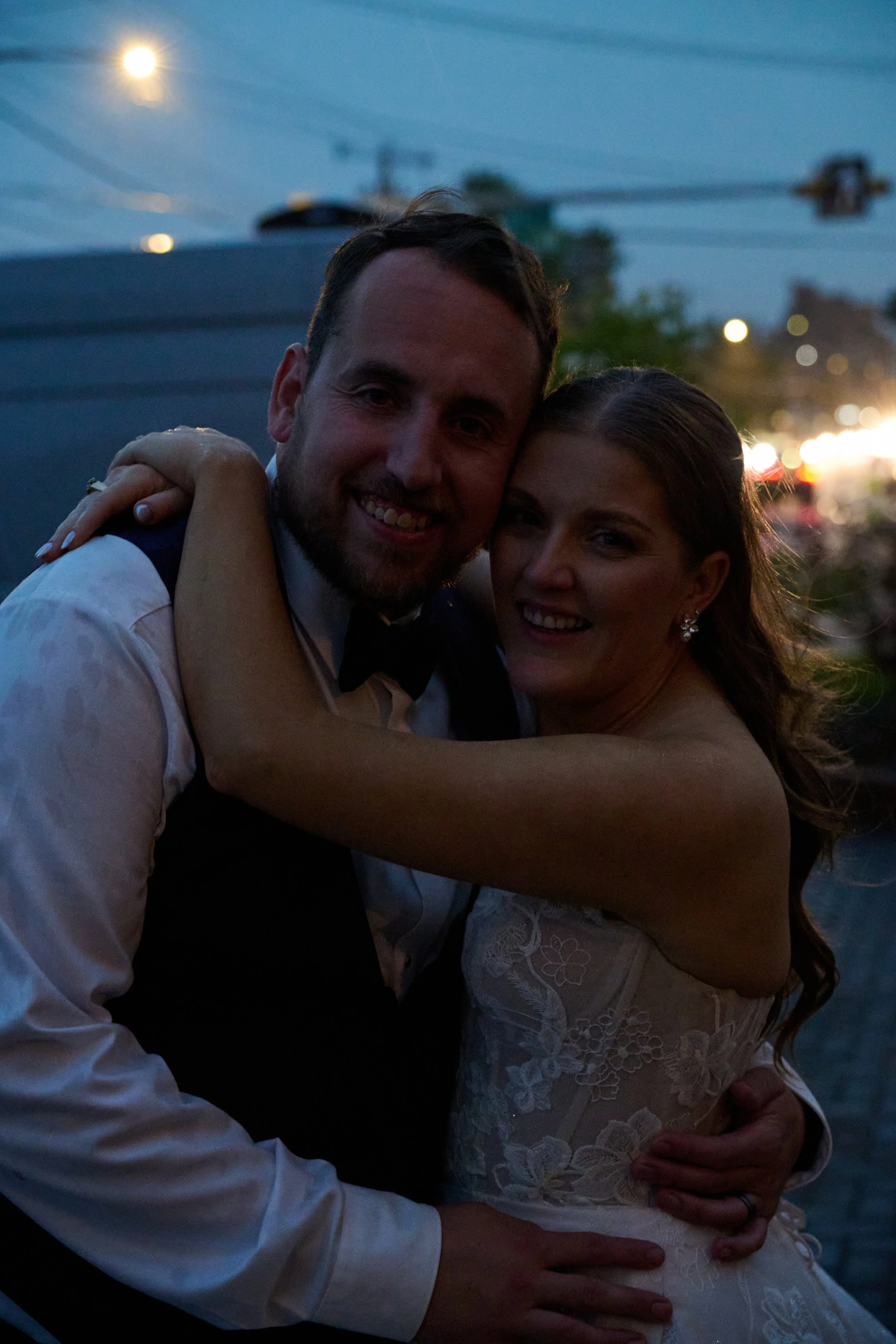 A newlywed couple embracing and smiling in an outdoor setting during dusk.