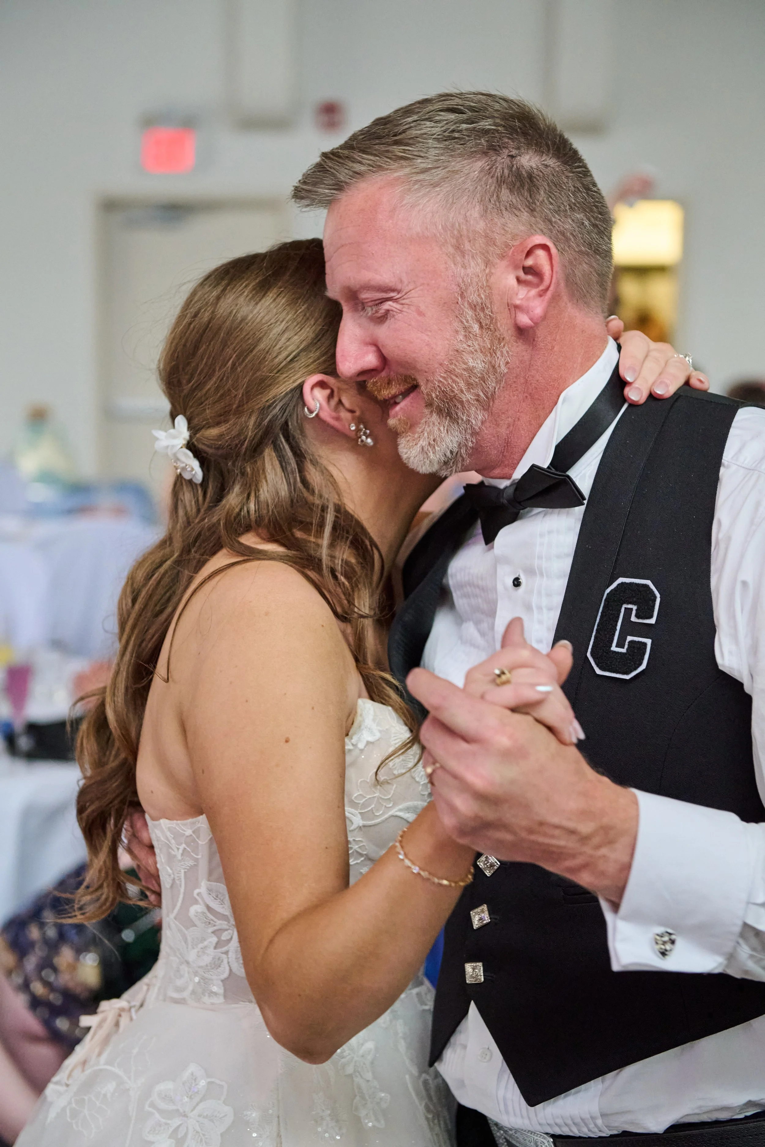 A bride and groom sharing a dance at a wedding reception, smiling and embracing.