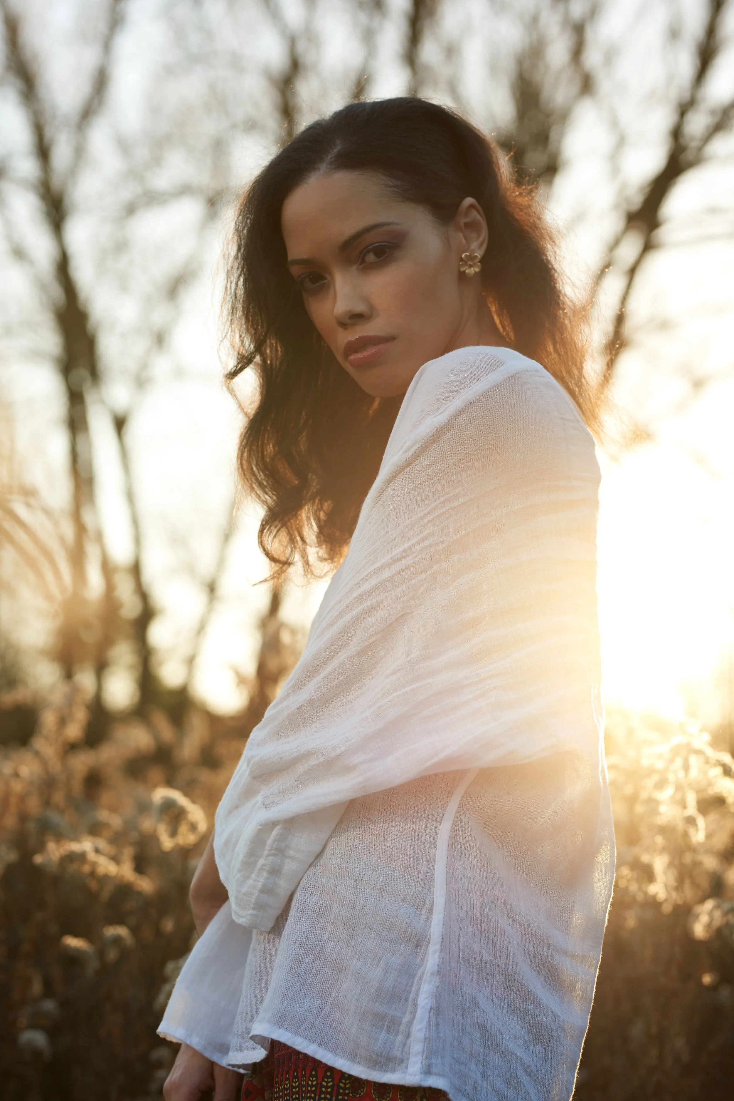 Woman in white shirt standing in a sunlit field during golden hour.