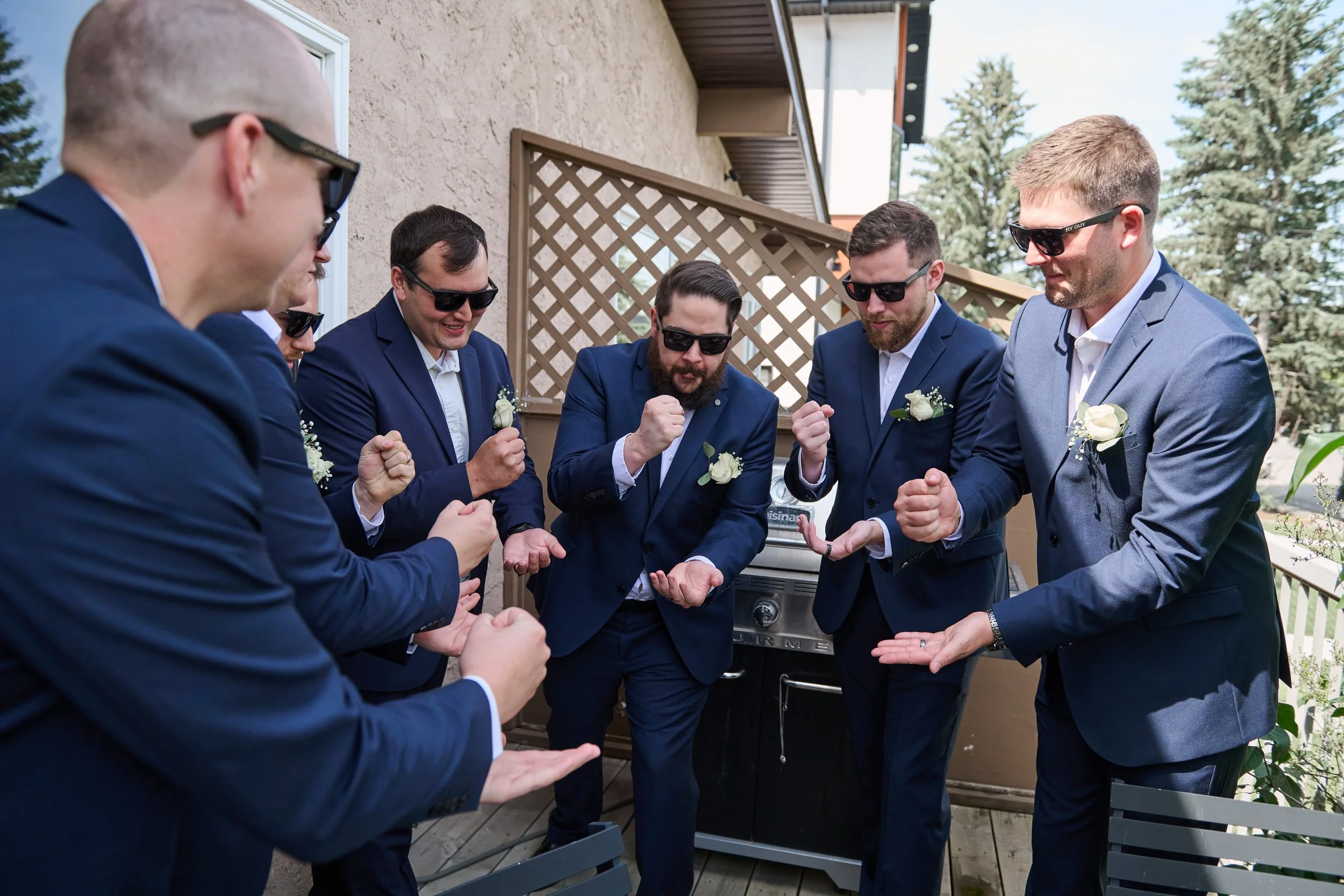 Group of six men wearing blue suits and sunglasses celebrating together outdoors on a balcony.