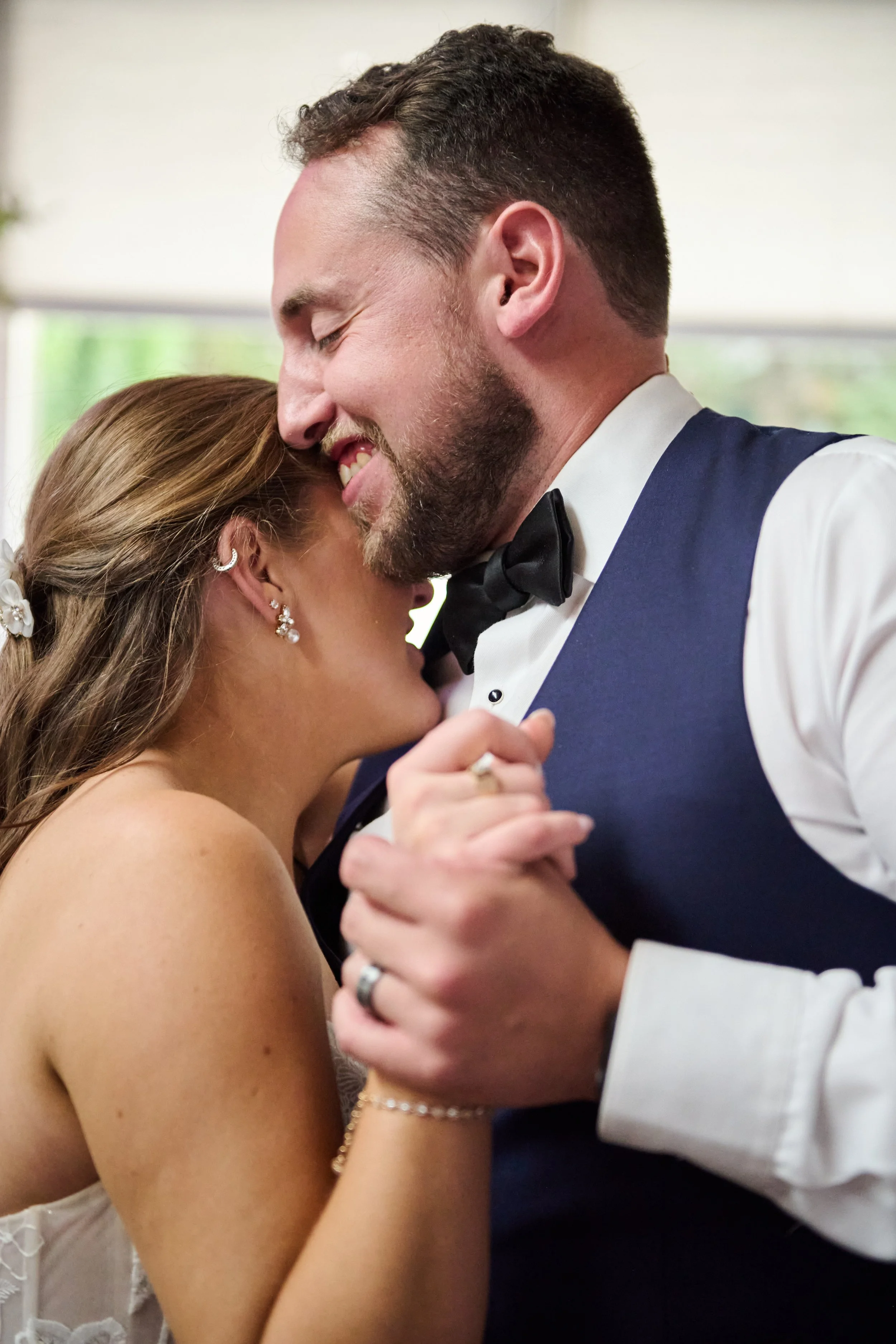 A bride and groom sharing a dance at their wedding, smiling with eyes closed and holding each other's hands.
