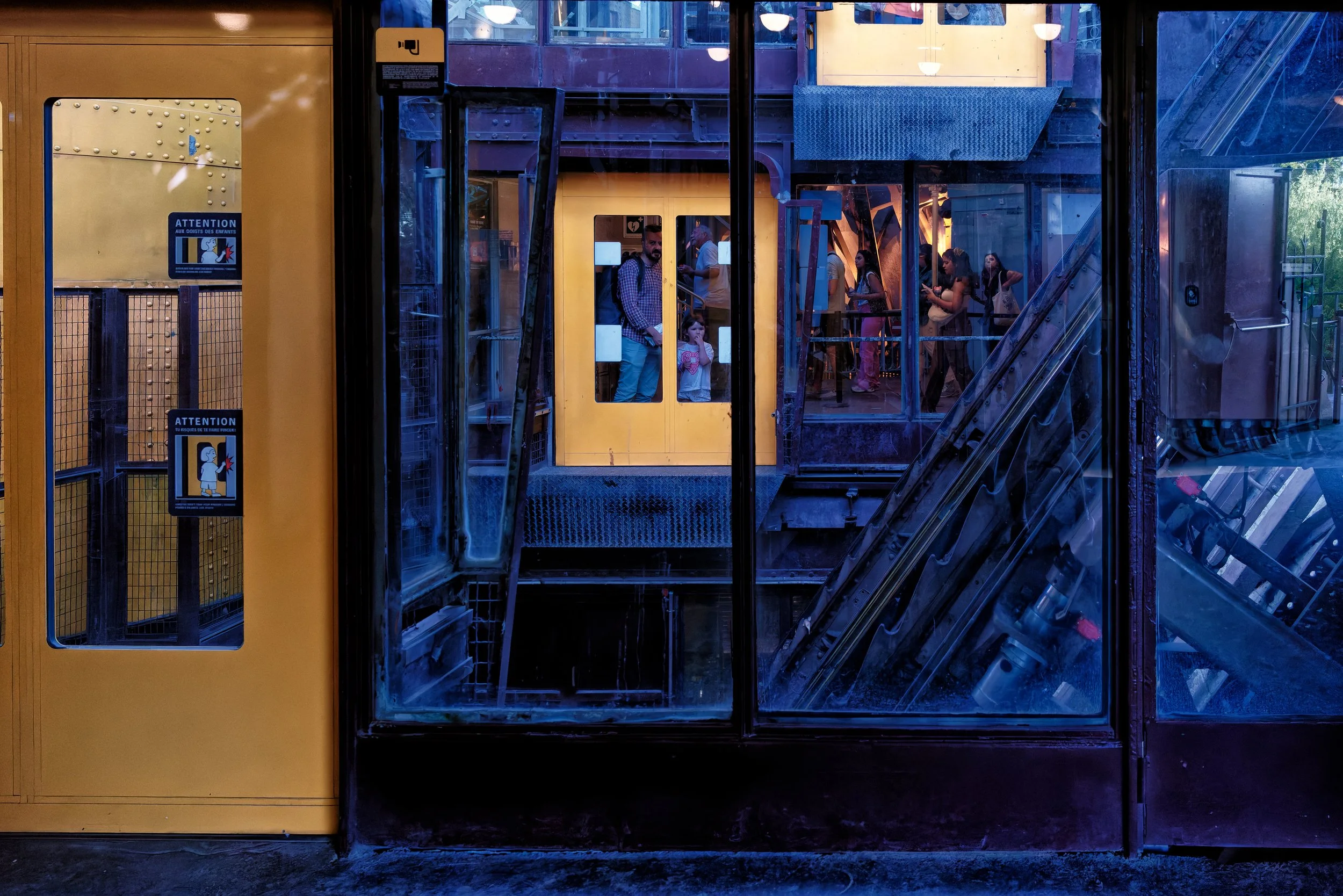 Passengers framed by a bright yellow train door and windows on an elevated platform in the Eiffel Tower.