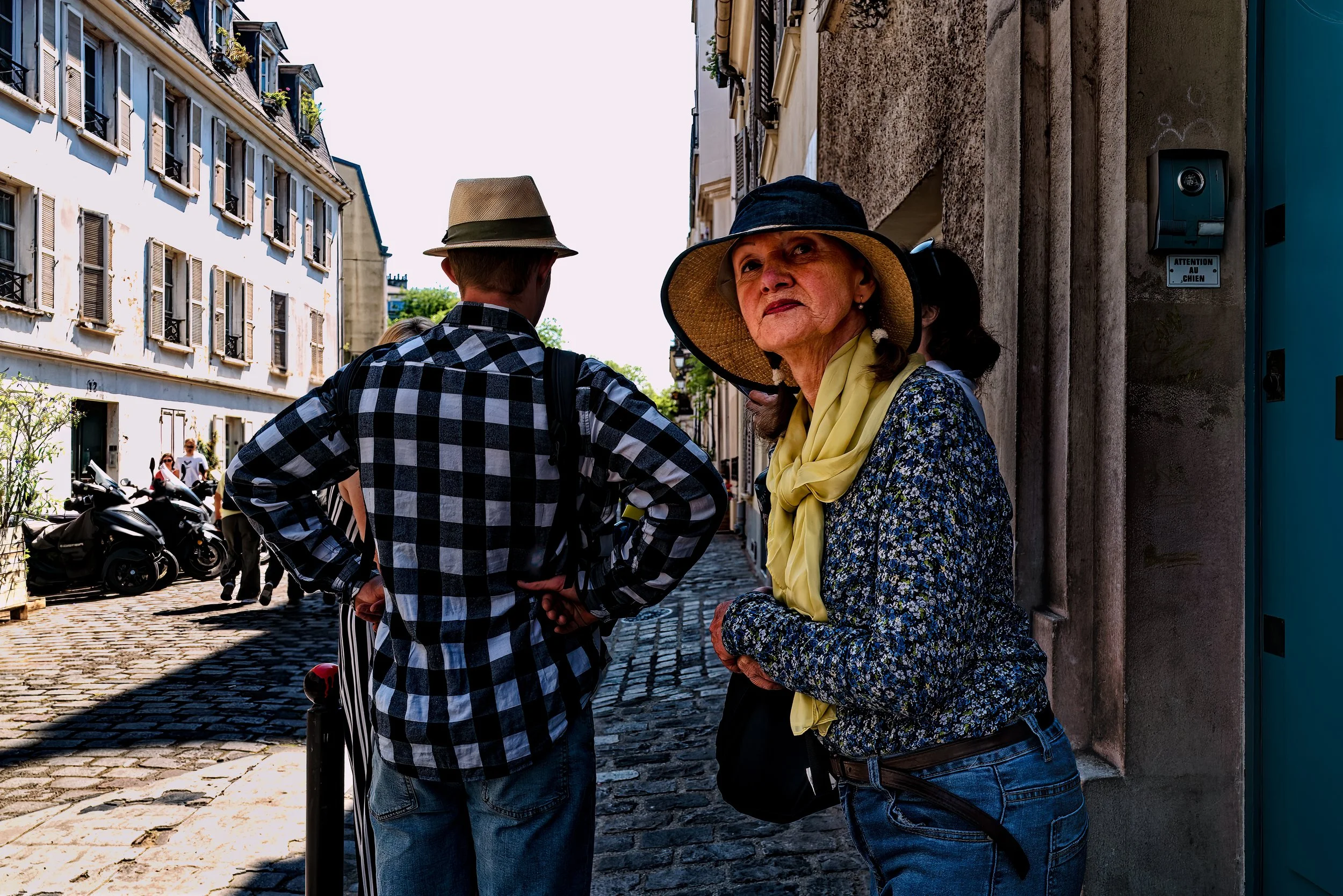Attention
On a sunlit Paris street, a woman turns toward the camera while the man beside her faces away, hands planted firmly at his hips. Their opposing gestures create a small tension within the frame—one figure open to the moment, the other absorb