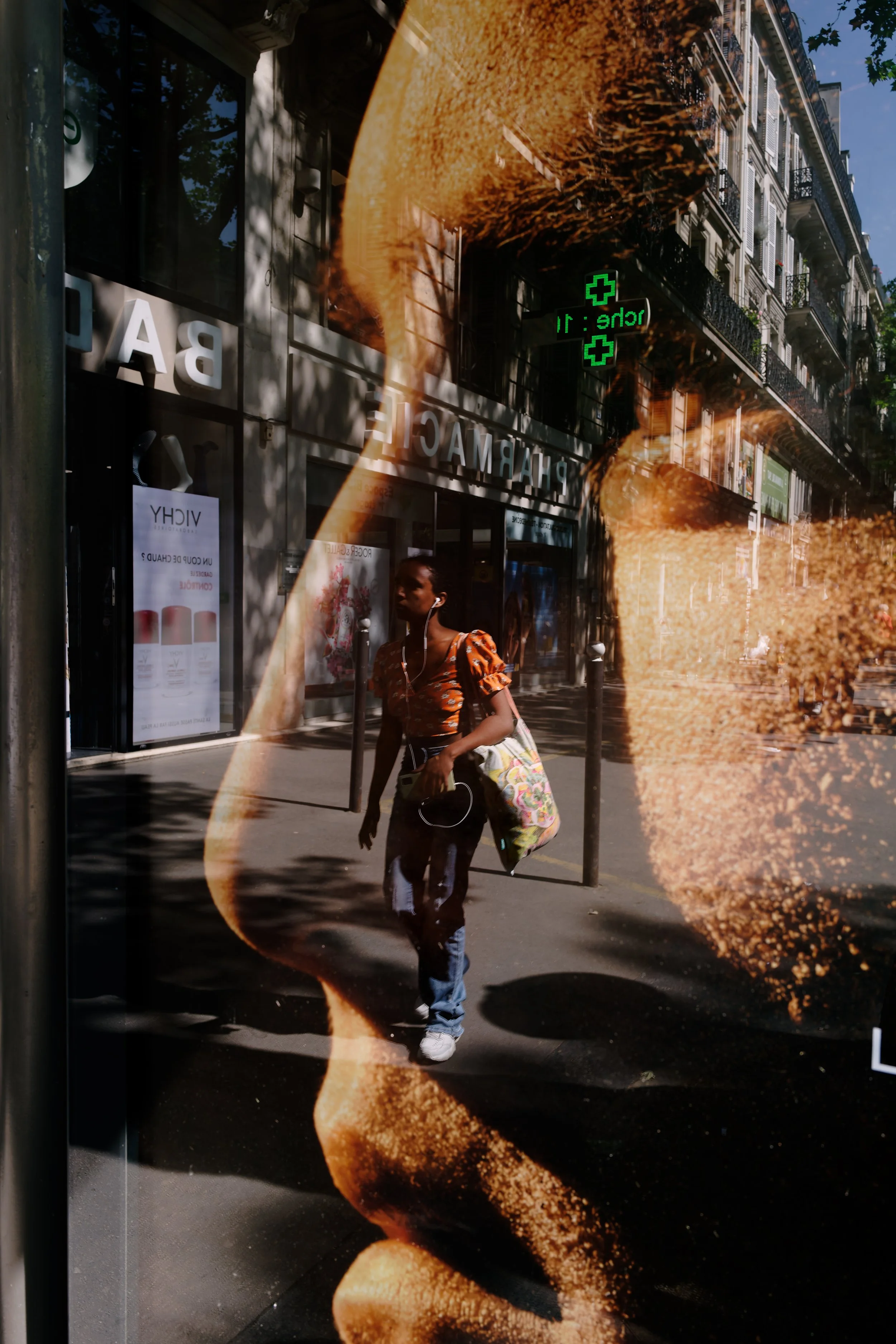 Paris in Profile
A pedestrian passes through the reflected profile of an oversized advertisement, briefly merging the human scale of the street with the commercial image behind the glass. The layered surface turns an ordinary walk into a moment where