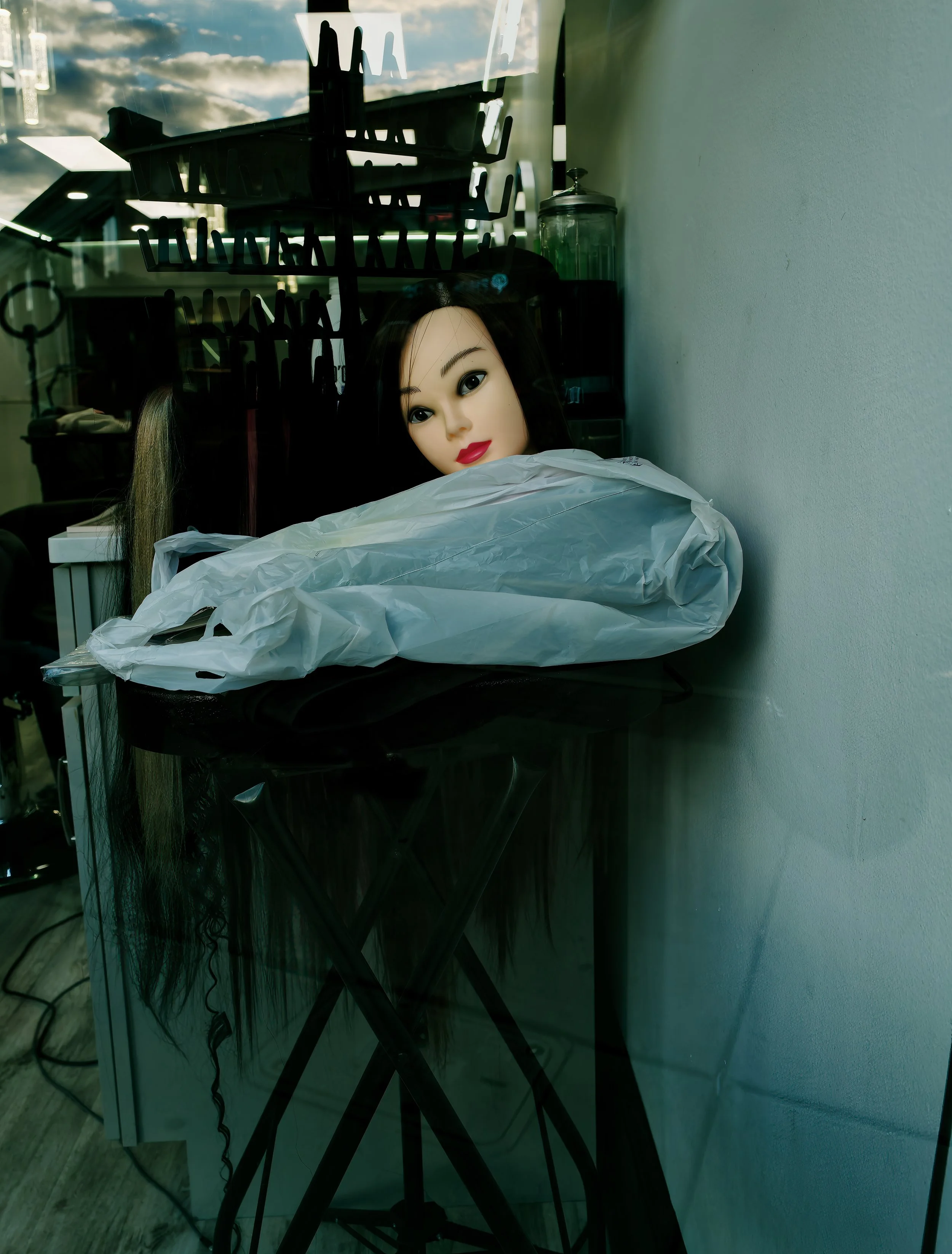 Mannequin head and wrapped plastic resting on a dark surface in a dim interior, creating a quiet still life of artificial human presence.